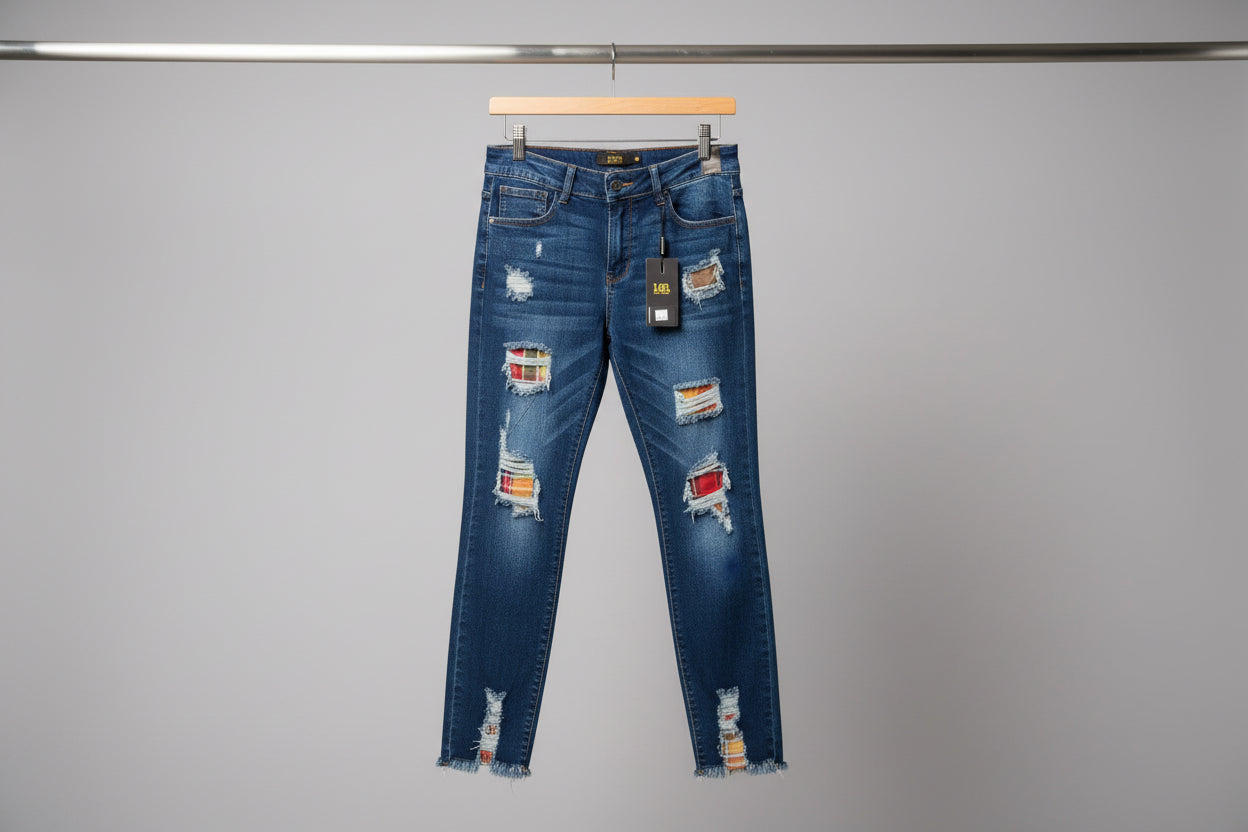 Medium blue mid rise skinny jeans with distressed patches featuring raw hem and striped fabric accents hanging on wooden hanger