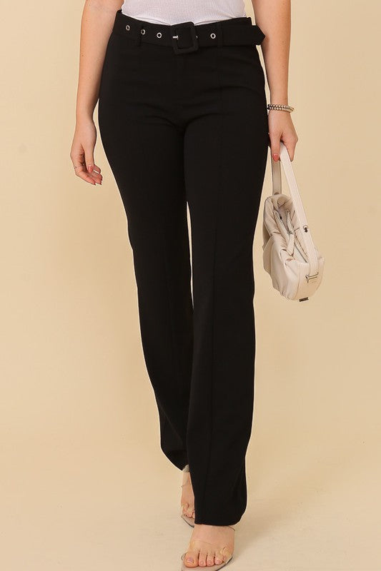 Woman wearing black high-rise belted straight-leg trousers paired with clear heeled sandals and carrying a beige purse