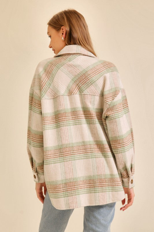 Woman wearing an oversized plaid shacket in soft green and beige tones paired with light blue jeans shown from the back