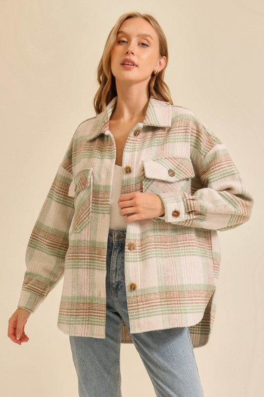 Woman wearing a long sleeve oversized plaid shacket in beige, green, and brown tones paired with blue jeans