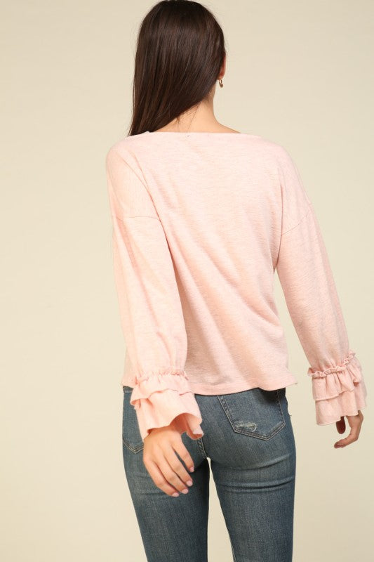 Woman wearing a soft pink long sleeve top with double layered ruffle cuffs and relaxed fit paired with blue jeans