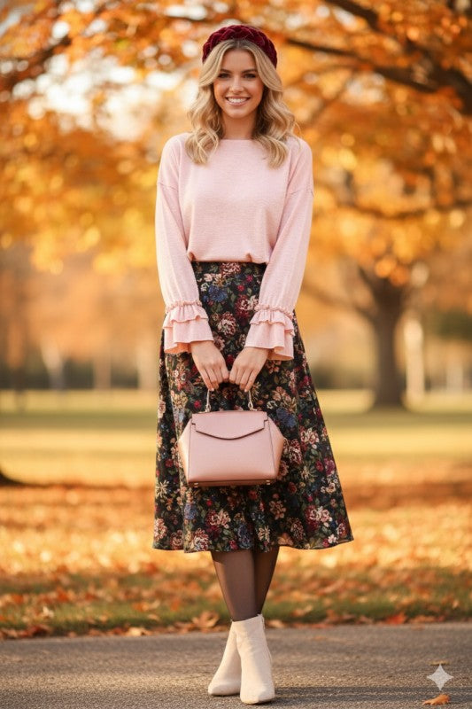 Woman wearing a light pink ruffle cuff long sleeve top paired with a floral midi skirt and beige ankle boots outdoors