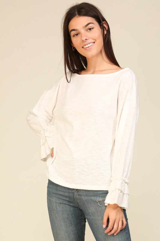 Woman wearing a relaxed fit white long sleeve top with ruffle cuffs and boat neckline paired with blue jeans