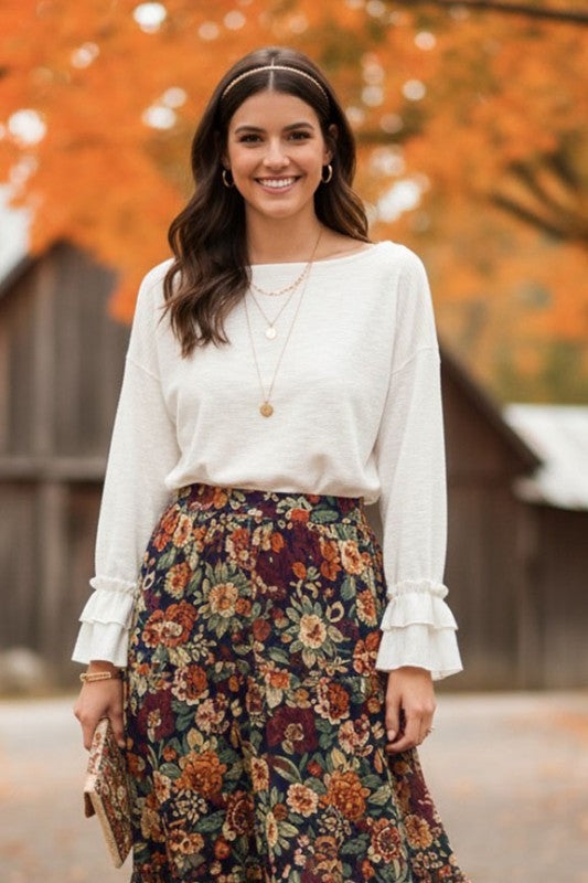 Woman wearing an off-white ruffle cuff long sleeve top with a relaxed fit paired with a floral autumn skirt outdoors