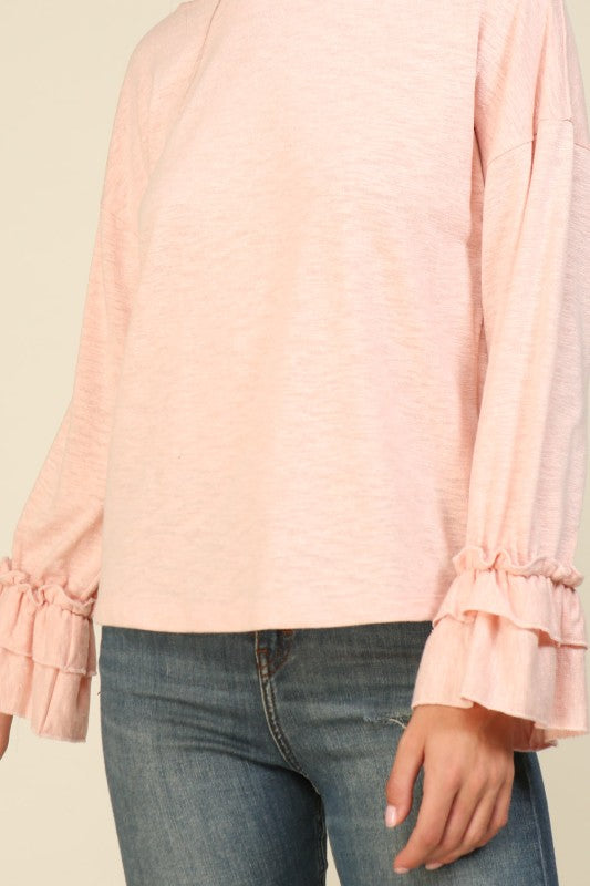 Woman wearing a soft pink long sleeve top with layered ruffle cuffs and a relaxed fit paired with blue jeans
