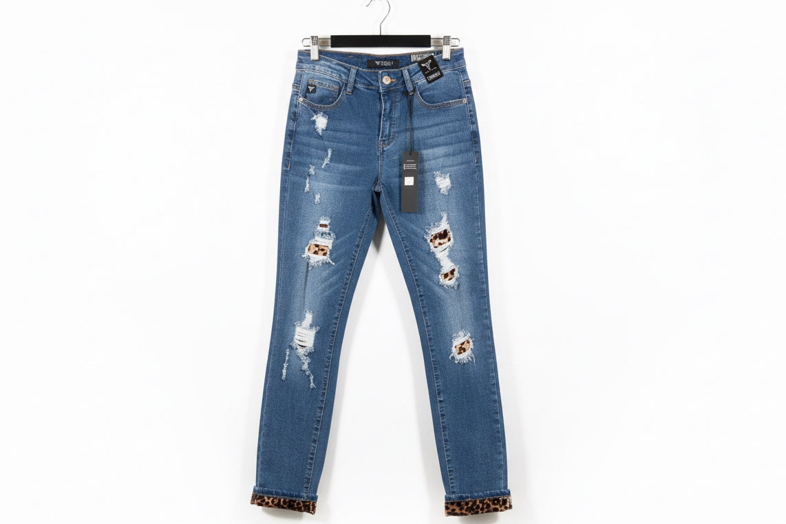 Medium blue mid rise skinny jeans with distressed patches and leopard print trim on cuffs hanging on black hanger