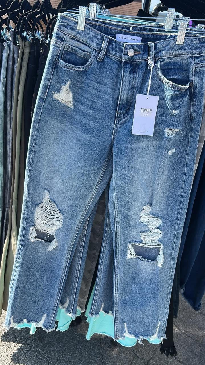 Blue distressed Flying Monkey jeans with raw frayed hems hanging on a rack outdoors in sunlight