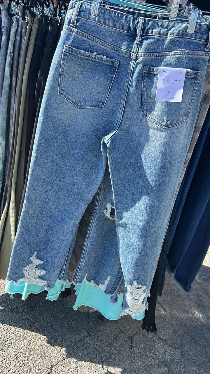 Pair of light blue distressed Flying Monkey jeans with raw frayed hems hanging outdoors in natural light
