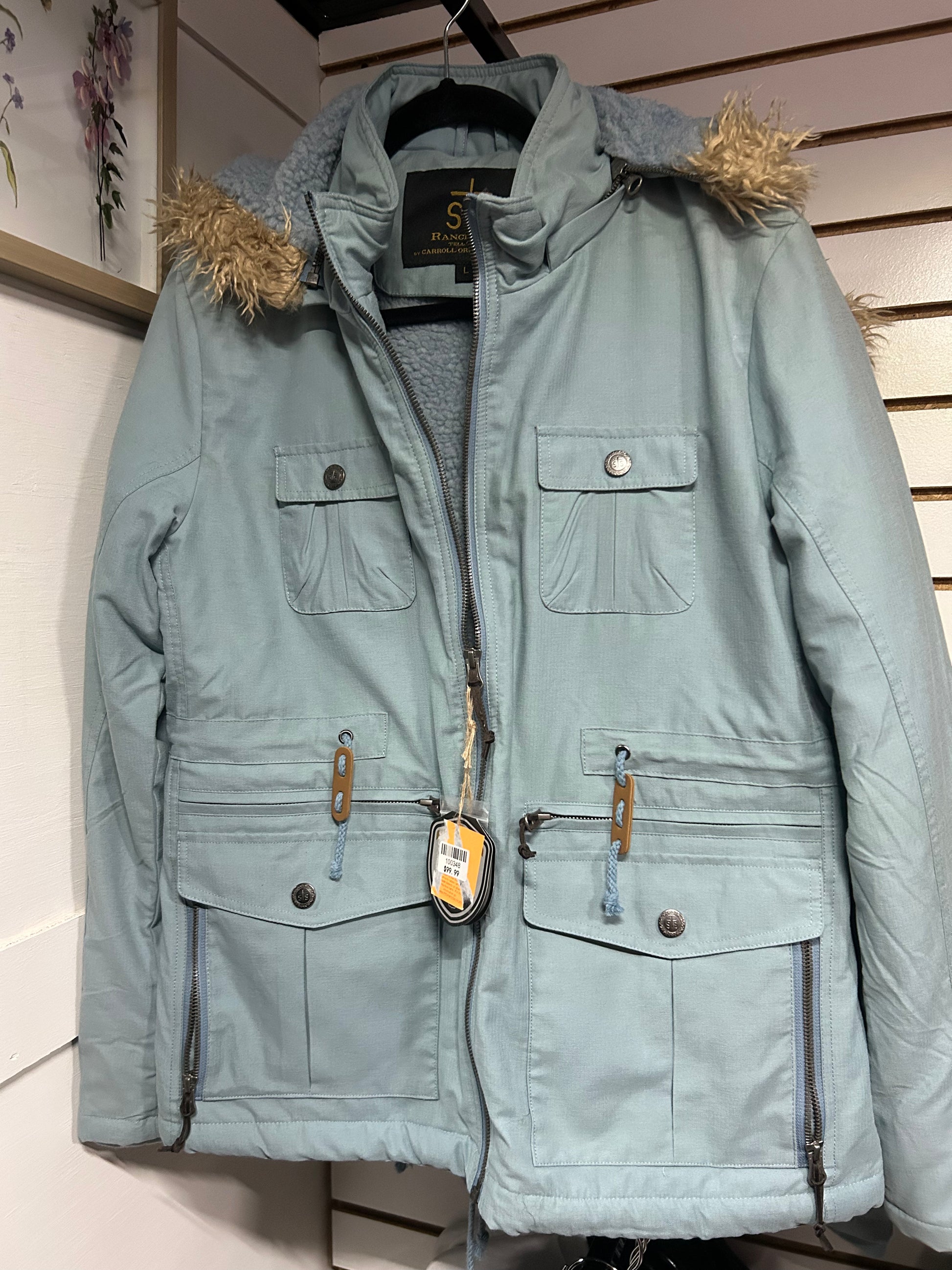 Light blue STS Ranchwear coat with faux fur trim on hood and multiple front pockets hanging on a black hanger