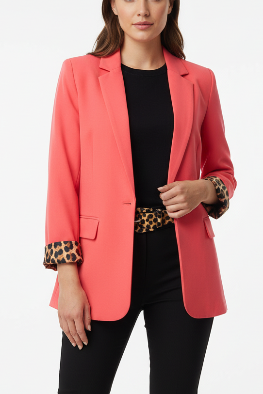 Woman wearing a coral blazer with leopard print lining on cuffs and matching leopard belt over black top and pants