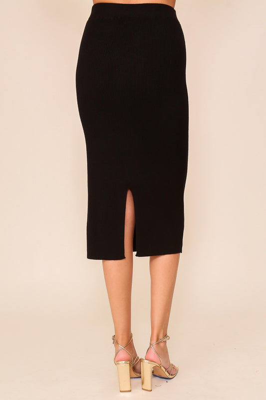 Back view of a black ribbed knit high-waisted sweater skirt with a center back slit worn with gold strappy heels